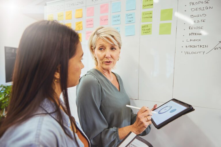 Woman talking to fellow while writing on a white board