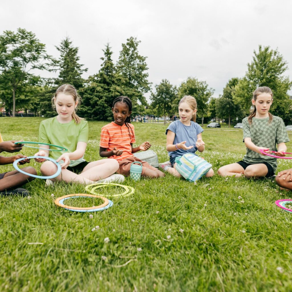 kids sitting next to each other in grass, playing with rings